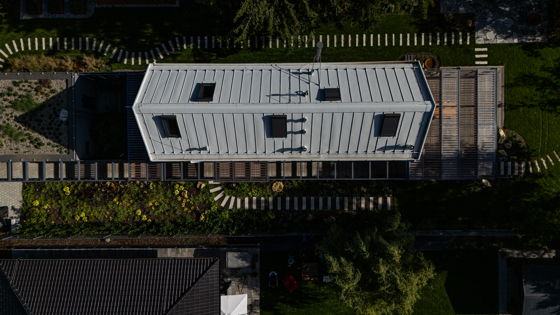 Top-down aerial view of a narrow timber house with a silver metal roof on a narrow plot